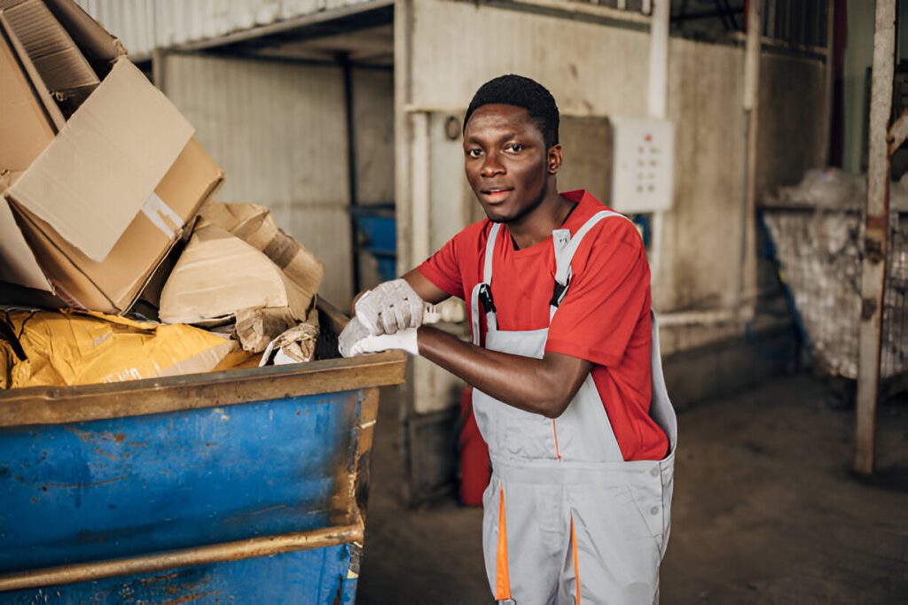 Portrait of a young male worker at recycling centre standing near the dumpster